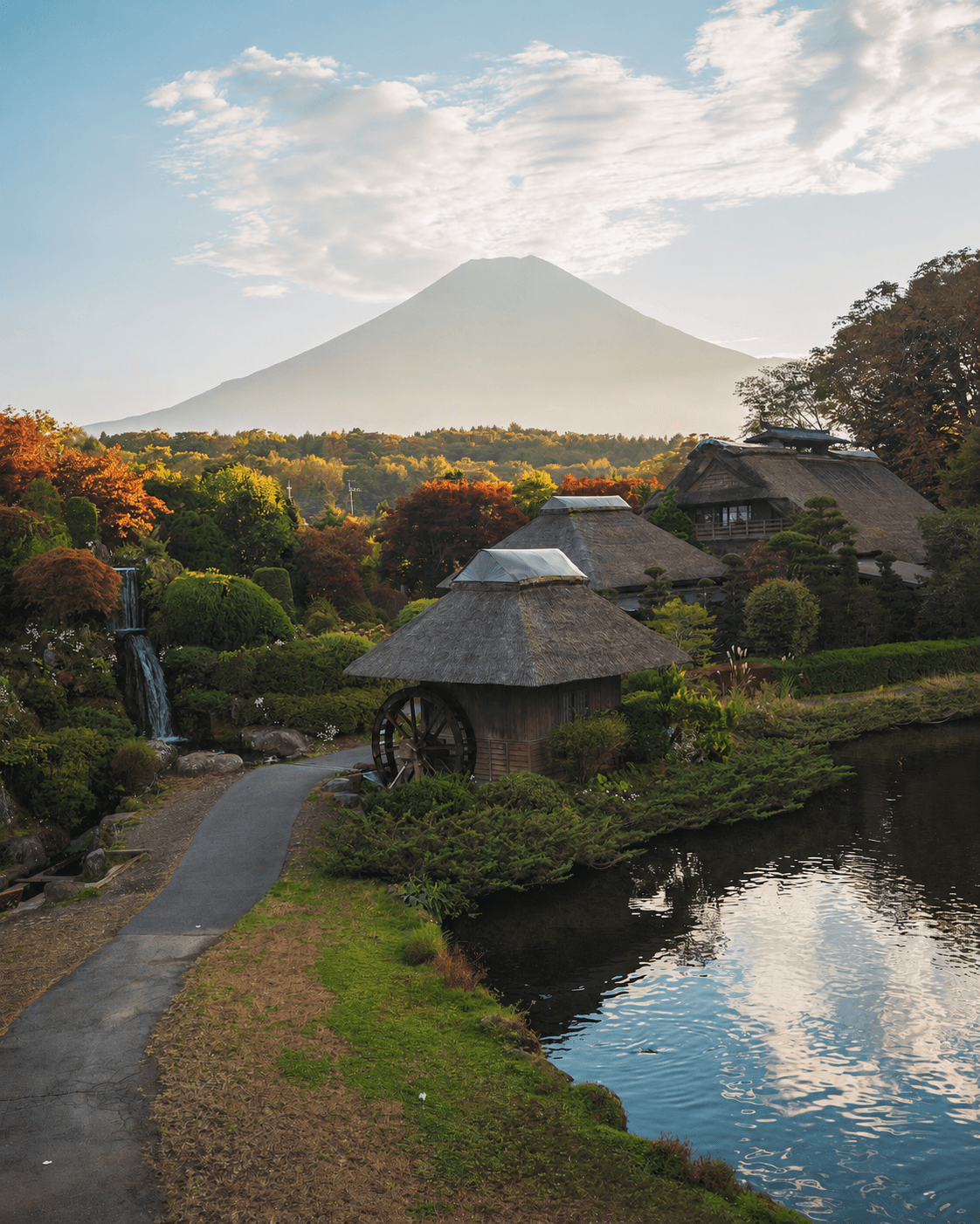 Traditional Japanese village with thatched-roof houses and a water wheel under a majestic Mount Fuji.