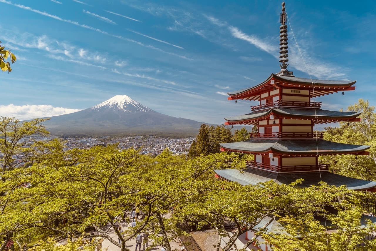 Chureito Pagoda stands among green trees with snow-capped Mount Fuji under a bright blue sky.